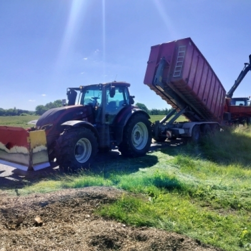 Traktor med kroghejsvogn og frakørselsvogn aflæsser container ved transport og bortkørsel af materiale.